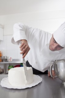 Hispanic chef spreading icing on side of cake
