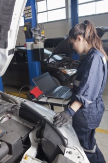 Hispanic mechanic diagnosing car engine with laptop
