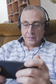Curious Hispanic man listening to cell phone with headphones