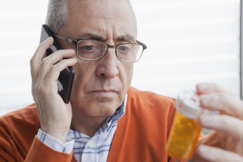 Serious Hispanic man talking on cell phone holding prescription bottle