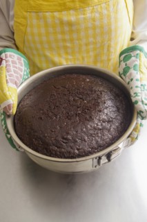Hispanic woman holding cake in pan with oven mitts