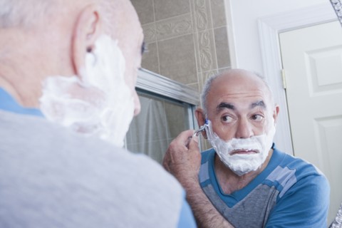 Reflection of Hispanic man shaving face in mirror