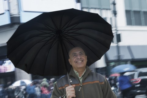 Smiling Hispanic man holding umbrella in city