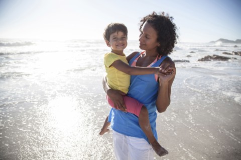 Mixed race mother carrying daughter on beach