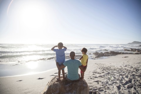 Mixed race father and children sitting on beach