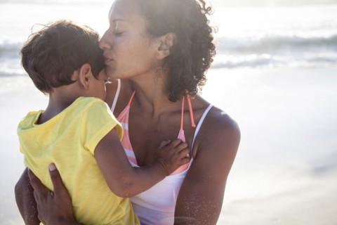 Mixed race mother kissing daughter on beach