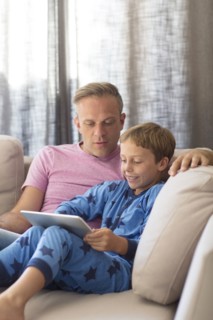 Caucasian father and son using digital tablet on sofa