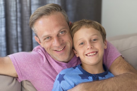 Caucasian father and son hugging on sofa