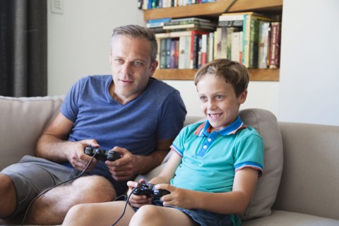Caucasian father and son playing video games on sofa