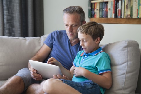 Caucasian father and son using digital tablet on sofa
