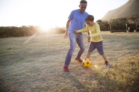 Caucasian father and son playing soccer in field