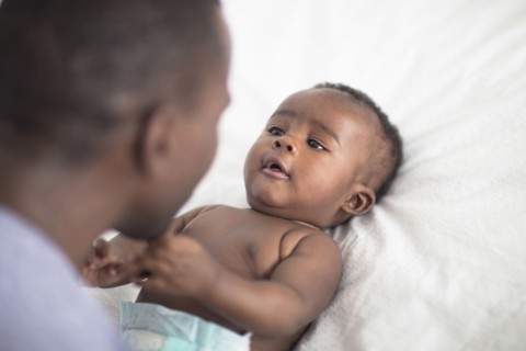 Close up of Black father playing with baby on bed