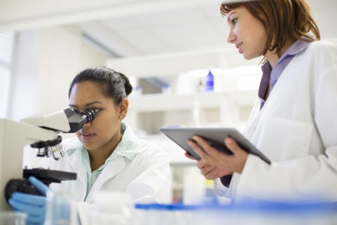 Scientists using digital tablet and microscope in laboratory