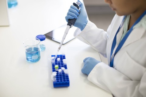 Mixed race scientist pipetting sample into tube in laboratory