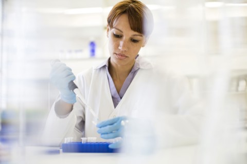 Mixed race scientist pipetting sample into tube in laboratory