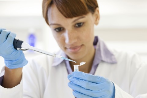 Mixed race scientist pipetting sample into test tube in laboratory
