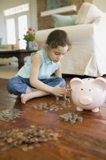 Young girl counting money next to piggy bank
