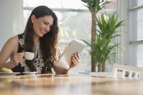 Hispanic woman drinking coffee and using digital tablet