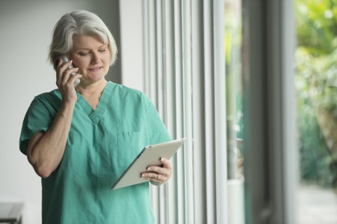 Caucasian surgeon in scrubs using cell phone and digital tablet