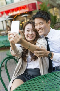 Korean couple taking cell phone photograph at sidewalk cafe