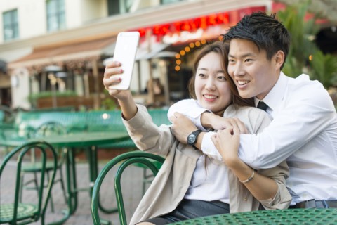Korean couple taking cell phone photograph at sidewalk cafe
