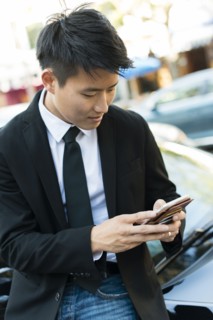 Korean businessman using cell phone near car