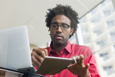 Hispanic businessman writing notes at glass office desk