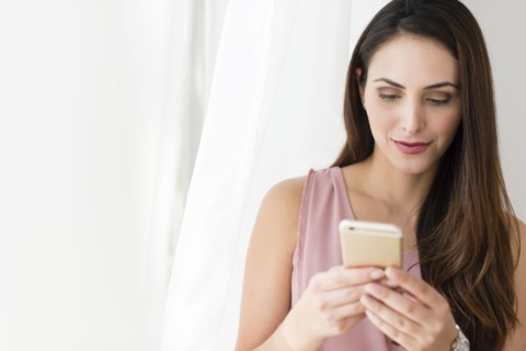Businesswoman using cell phone near curtain