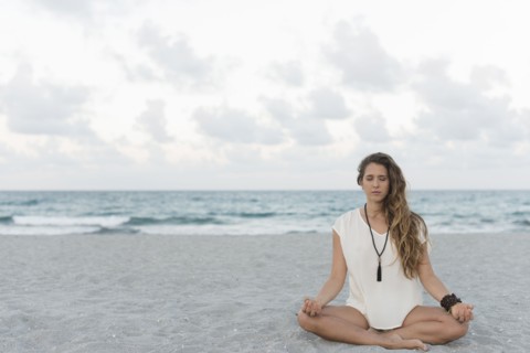 Hispanic woman meditating on beach