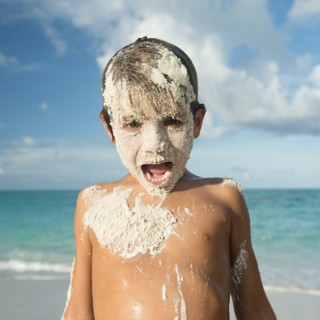 Hispanic boy covered in sand on beach