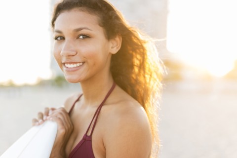 Mixed race teenage girl carrying surfboard on beach