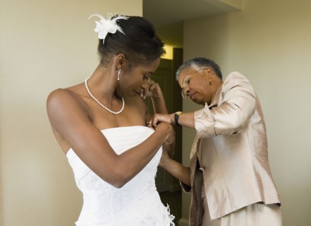 African mother helping bride with wedding dress