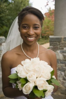 African bride holding rose bouquet and smiling