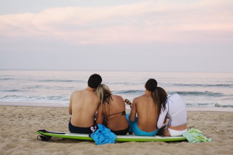 Teenage couples sitting on surfboard on beach