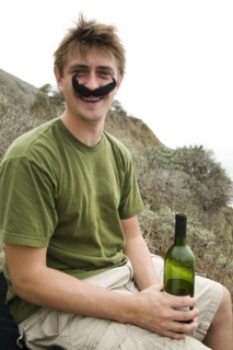 Caucasian man in costume mustache holding wine bottle
