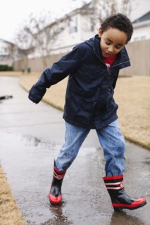 Mixed race boy splashing in rainboots
