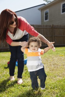 Mother helping baby walk in backyard