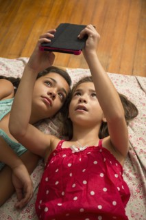 Mixed race sisters using digital tablet on bed