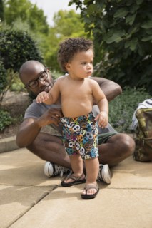 Father adjusting toddler son's shorts in park