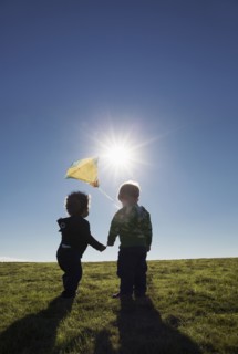 Boys watching kite flying against blue sky