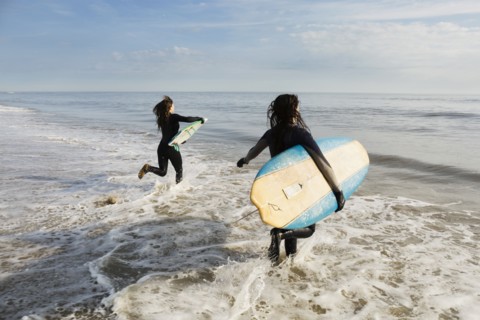 Surfers carrying boards in waves