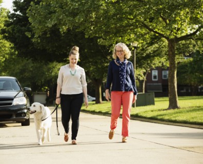 Caucasian mother and daughter walking dog on suburban street