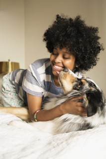Mixed race woman playing with dog on bed
