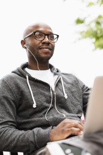 Black man using laptop and earphones outdoors