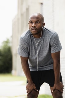 Black runner resting in city with earbuds
