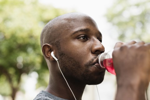 Black runner drinking juice in city with earbuds