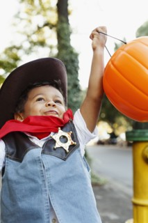 Mixed race boy dressed as cowboy holding pumpkin pail for Halloween
