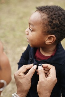 African American mother buttoning sweater of son