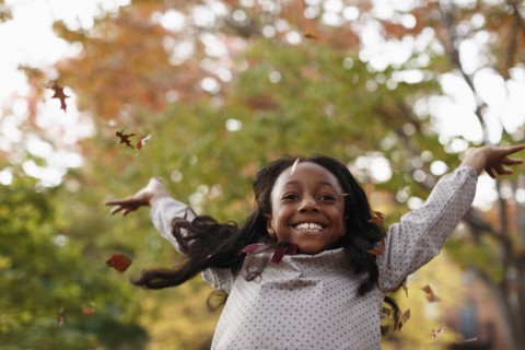 Low angle view of African American girl playing in autumn leaves