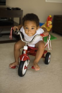 Mixed race boy riding tricycle in living room